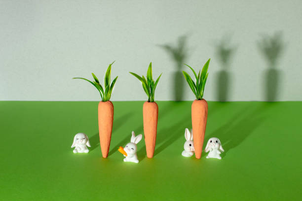 istock Carrots with little white bunnies on gray and green background. Minimal Easter concept. Spring minimal composition. 2198058329
