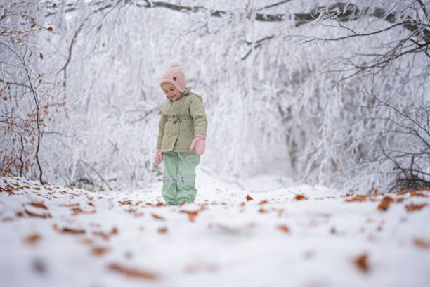 Health benefits of winter play outdoors in snow for children. Happy girl holding big snowballs and laughing in the first snow, doing a snowman in forest park.