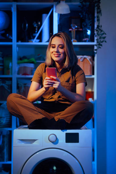 istock Woman Sitting on a Washing Machine Texting on her Mobile 2198070942