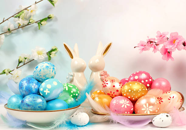 Abstract Easter composition with pink, gold, blue decorated eggs in cups, feathers and flowering branches. Happy Easter concept. Banner for the screen with space for congratulatory text,