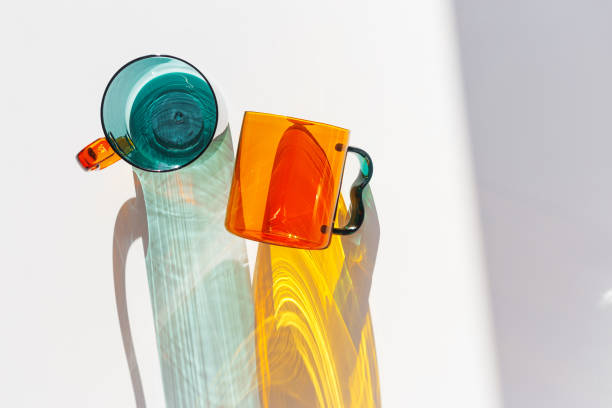 istock Orange and green Glass Mugs with bright sunlight Shadows, transparent cups casting dynamic, vibrant lights reflections and shadows on light white, creative aesthetic top view, minimal style, closeup 2198098268
