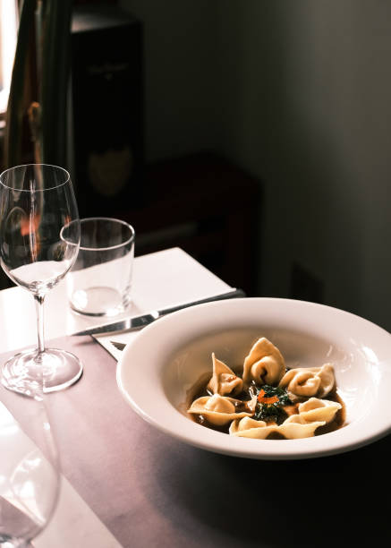 istock Elegant Italian tortellini dish served in a light broth with fresh herbs, fine dining setting with wine glasses on a wooden table, cozy ambiance in an authentic Italian restaurant, gourmet pasta experience 2198102600
