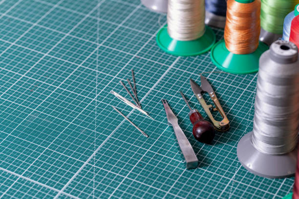 Thread bobbins for stitching leather and tanners tools on a cutting mat, copy space, selected focus. Workshop, tailor, handmade, workplace, craft, manual production, high quality concept.