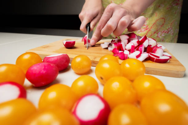 Close-up of cutting vegetables for making salad. Sliced yellow cherry tomatoes and red radishes