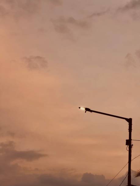 A vintage street lamp stands tall against the fading hues of an orange twilight sky. As daylight dims, the warm glow of the sunset blends into the approaching night, creating a nostalgic and cinematic ambiance.