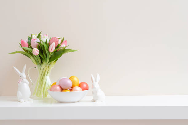 istock Colorful Easter eggs, spring tulip flowers and ceramic bunny figurines on white table over plain wall background 2198108292