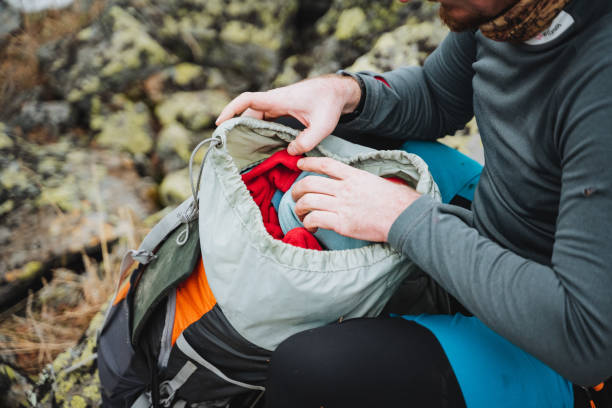 A man sits on rock, leisurely packing backpack in outdoor landscape