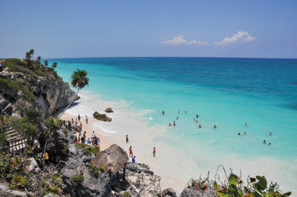 Tulum, Mexico- May 16, 2013: The Mayan city of Tulum stands 130 km south and 700 years away from Cancun. Tulum was once a mighty walled city built by the Mayan people. The Tulum Ruins are one of the most well preserved Mayan sites along Mexico’s coast and provide a glimpse of how the Mayans lived and why they were a renowned civilization. This impressive Tulum archaeological site sits on the edge of a steep cliff. It overlooks the gorgeous Caribbean Sea. Right below the site lies the Tulum Ruins Beach, one of the area’s best beaches.  Here is the stunning beautiful beach below the ruins.