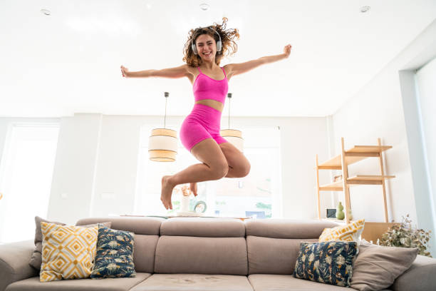 istock Beautiful young woman jumping on sofa at home 2198127257