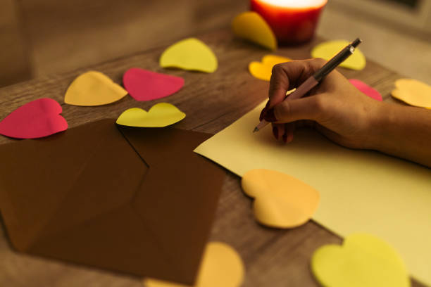 istock Hand Writing a Love Note with Heart-Shaped Paper Decorations on Wooden Table 2198127940