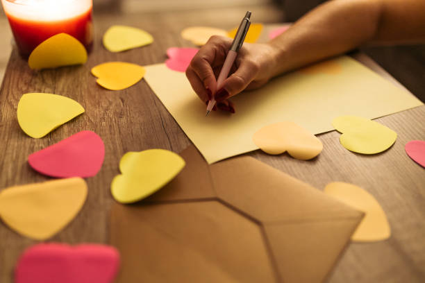 istock Hand Writing a Love Note with Heart-Shaped Paper Decorations on Wooden Table 2198127946