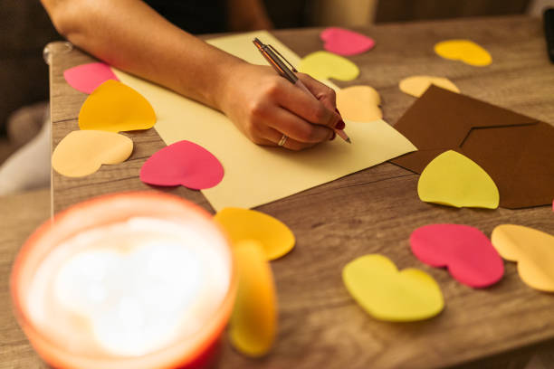 istock Hand Writing a Love Note with Heart-Shaped Paper Decorations on Wooden Table 2198127955