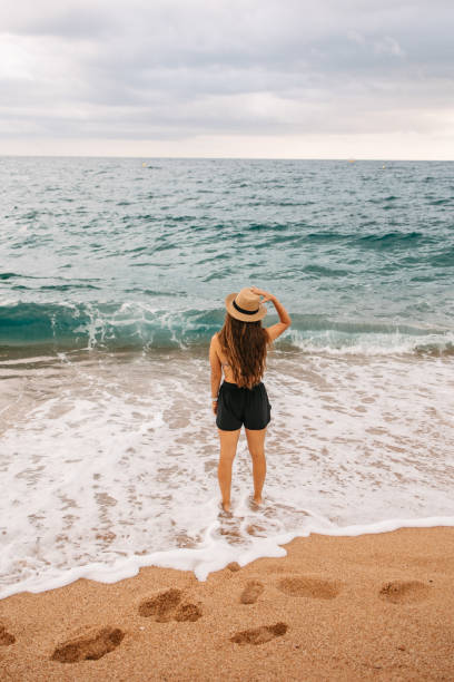A rear view of a woman with a hat on her head, standing in the sea