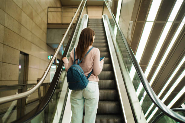 istock Young woman ascending escalator in modern building 2198130378