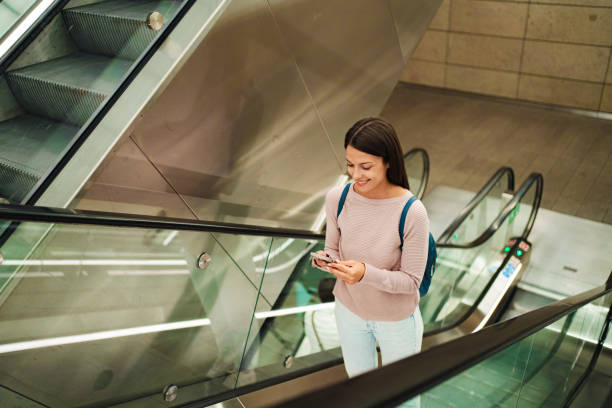 istock Smiling young adult using smartphone on escalator 2198130420
