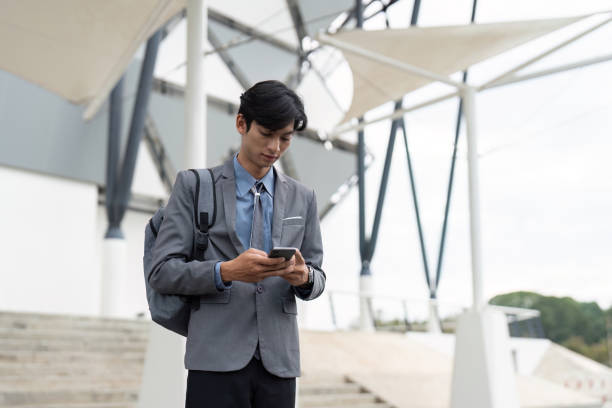 istock Young professional texting on smartphone outside a modern building, blending work and technology. 2198130622
