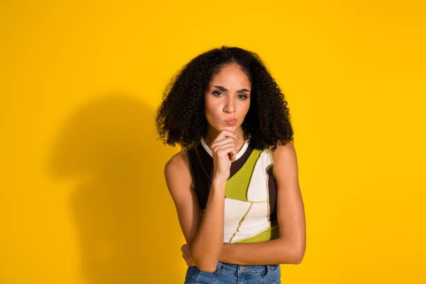 istock Confident young woman posing against a vibrant yellow background with a thoughtful expression and stylish casual attire 2198132517