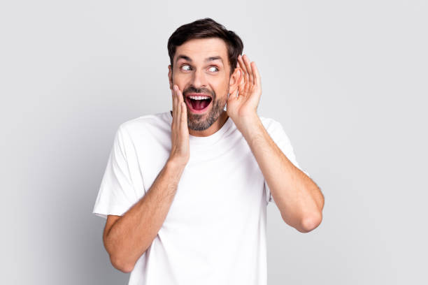 istock Young cheerful man in casual style making a fun gesture with hands near ears, expressing surprise and excitement, on a light background 2198133742