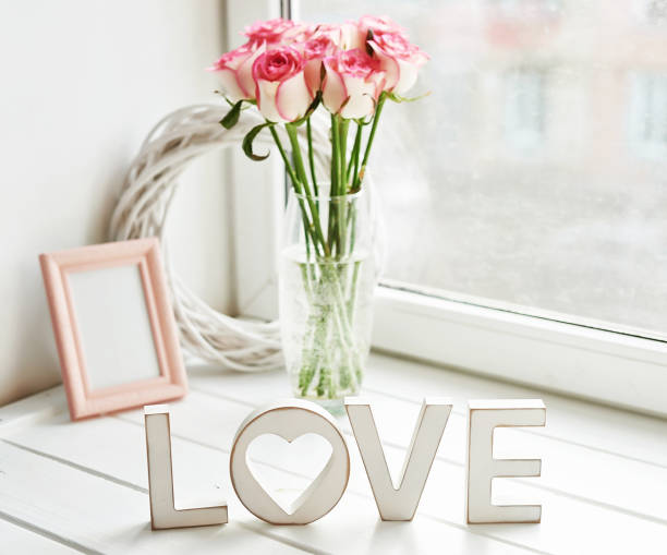 istock Valentine Card. Composition with fresh roses and photo frame on window sill. Space for text. Floral composition with inscription Love. Mother's day and March 8 card 2198133797