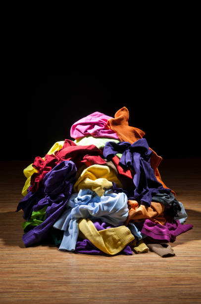 Huge pile of colorful clothes on wooden floor and black background. Household chores. The laundry needs to be ironed, folded, and put away in the closet.
