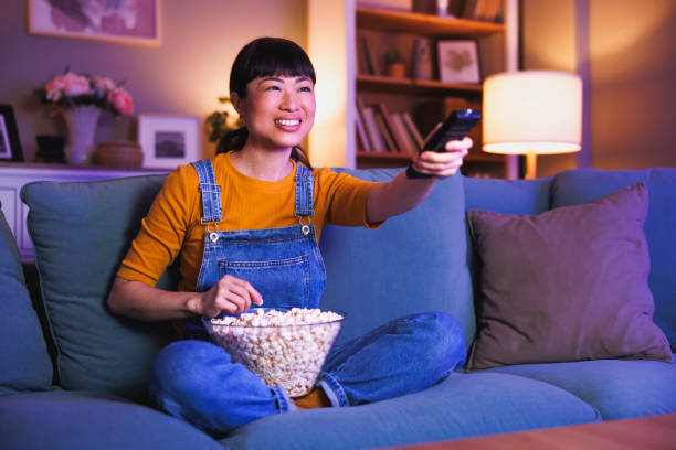 istock Woman turning on TV using remote control while relaxing at home late at night 2198143625