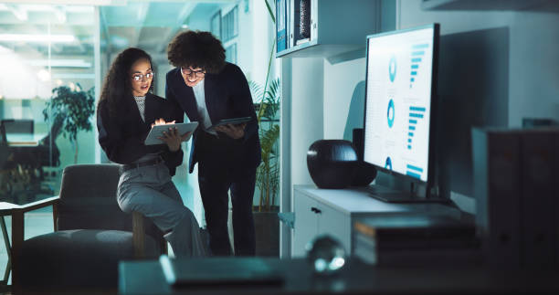 istock Office, business people and tablet for networking, internet research and sales graph. Overtime, man and corporate woman for online project management, reading email and night planning at agency 2198148911