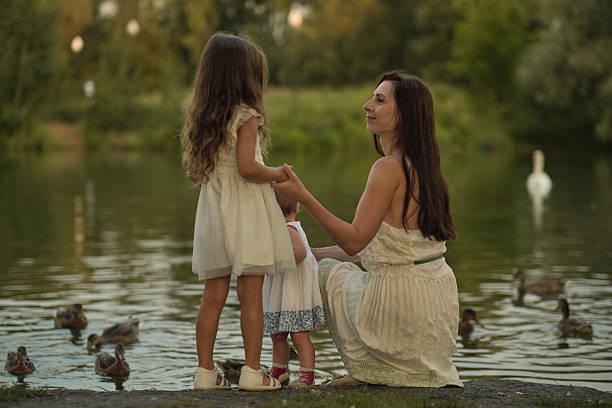 istock Mother and daughters by the lake, hands clasped, a bond evident. A serene moment reflecting the importance of family time in nature. 2198149607