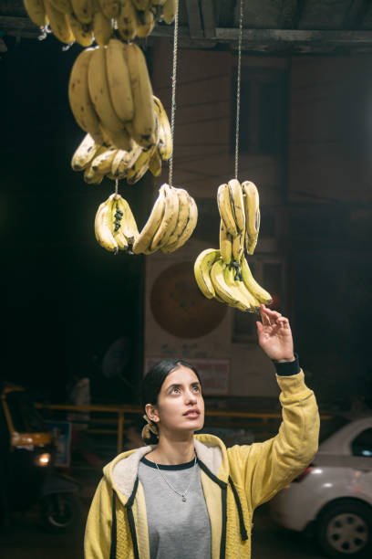 A young woman tries to select a bunch of bananas to buy from a roadside fruit shop.