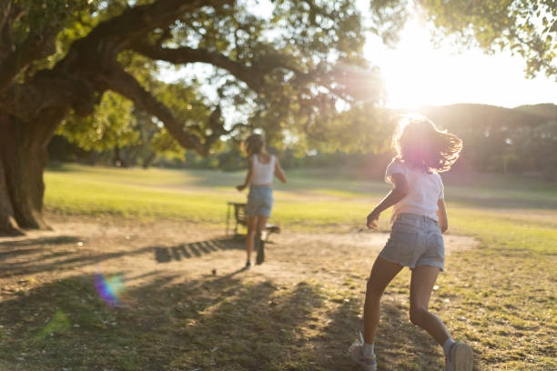 Kids playing energetically under a large tree at sunset
