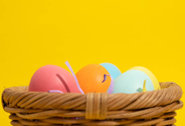 Extreme close up of multi colored easter eggs in a straw basket on a yellow background with copy space. Easter crafts concept