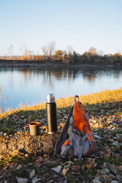 istock Nestled beside a tranquil lake, a trusted backpack is securely positioned near a sturdy thermos, an elegant cup, and a rugged mug, harmoniously blending with the surrounding natural beauty 2198184561