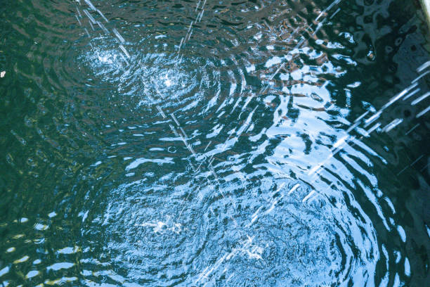 Close-up of water ripples forming concentric circles as droplets splash onto the surface of a garden fountain.