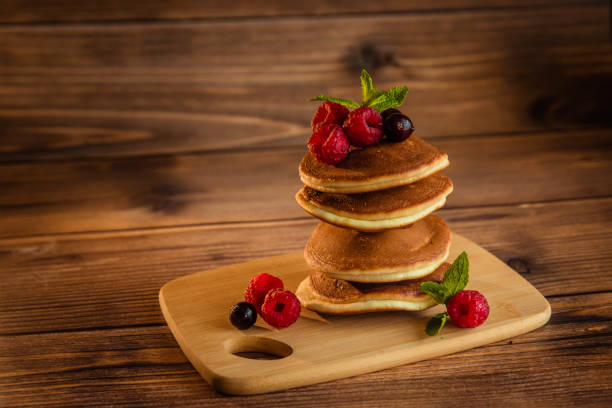 Appetizing pancakes with berries and powdered sugar on a wooden background.