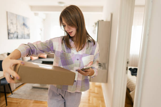 istock Woman using mobile phone and checking and opening  just received package boxes 2198195119