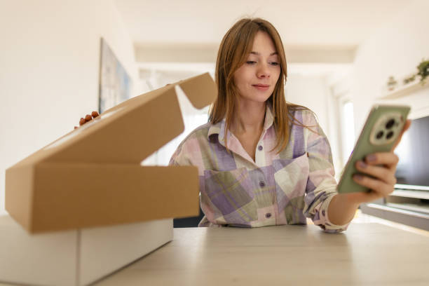 istock Woman using mobile phone and checking and opening  just received package boxes 2198195138