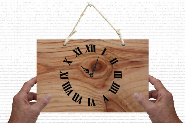 Hands holding a wooden clock hanging on a wall