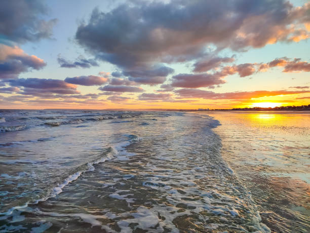 Golden sunset reflects on the ocean waves, creating a tranquil atmosphere with colorful clouds.