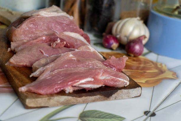 istock features sliced raw pork arranged on a wooden cutting board, alongside whole garlic and shallots on a tiled surface. 2198204417