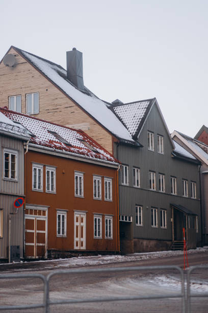 A street level view of Tromso featuring colorful buildings with snow and a metal railing along the sidewalk under a cloudy winter sky.
