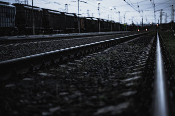 Railway tracks extending into the distance, shot in a dim atmospheric evening setting fronted by a striking foreground showing close-up details of gravel and rails.