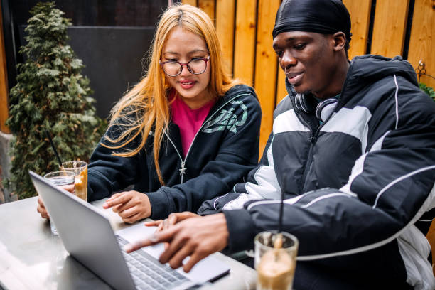 istock Friends enjoying having coffee at sidewalk cafe while looking at laptop 2198223842