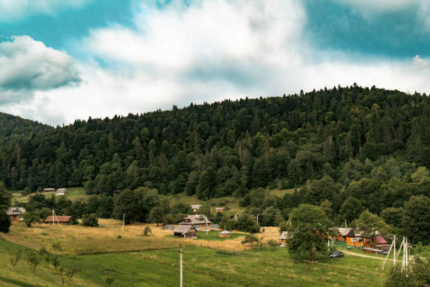 The green hills rise above a small, quiet village, where the beauty of nature embraces the simplicity of rural life. The scene radiates peace and calm under a bright blue sky.