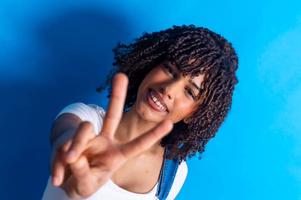istock Young woman showing peace sign on blue background 2198253734