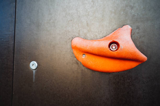 This image showcases a detailed closeup view of an orange climbing grip specifically designed for use on a climbing wall, highlighting its unique texture and vibrant color that stands out