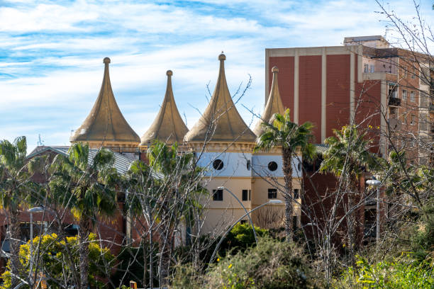 A distinctive building with four golden cone-shaped rooftops, surrounded by palm trees and greenery under a bright blue sky.