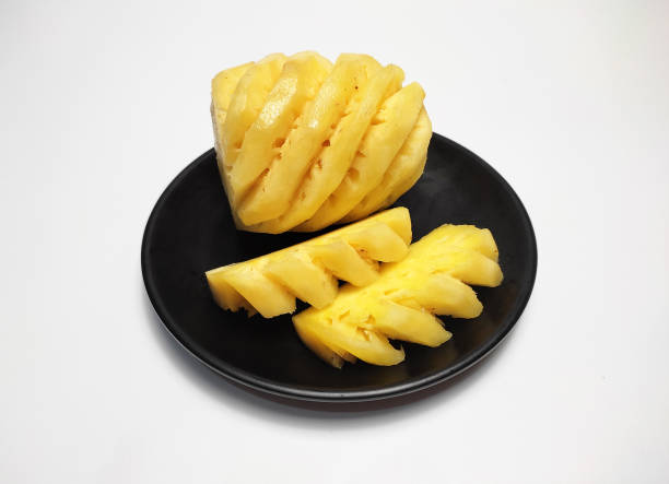 istock A whole pineapple and several pieces of pineapple, in black plate, isolated on white background 2198295898