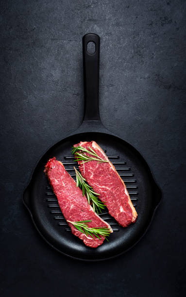 istock Raw beef sirloin steaks with medium mamory with rosemary on grill pan. Black background, top view 2198298645