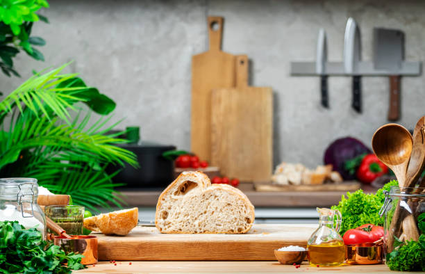 istock Cut whole grain wheat sourdough bread on wooden cutting board.. Kitchen table with vegetables and herbs against the background of modern classic kitchen 2198298656