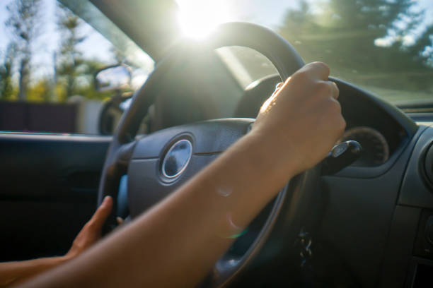 Girl is driving a car and traveling on a sunny day, close-up of her hands on the steering wheel. The woman is touring the country, doing a road trip and enjoying the life.
