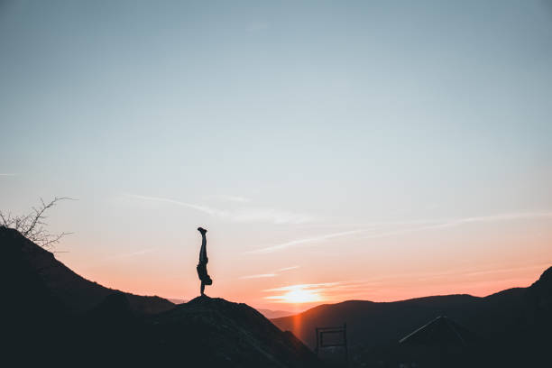 Man doing a handstand on high viewpoint balancing on mountain edge. Silhouette.
